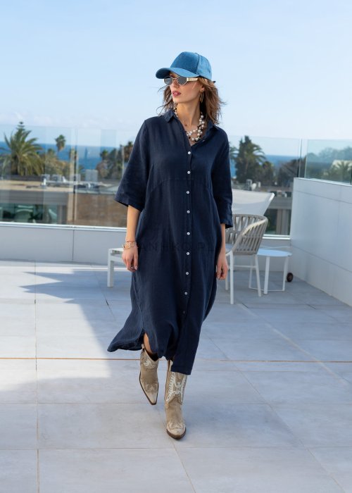 Granatowa lniana sukienka maxi w stylu szmizjerki, zapinana na guziki, o luźnym fasonie oversize, stylizowana z kowbojkami i czapką.