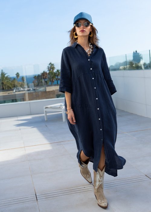 Granatowa lniana sukienka maxi w stylu szmizjerki, zapinana na guziki, o luźnym fasonie oversize, stylizowana z kowbojkami i czapką.