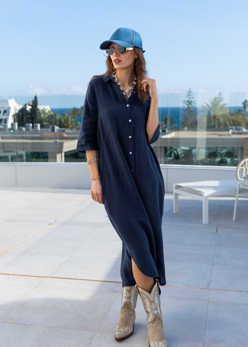 Granatowa lniana sukienka maxi w stylu szmizjerki, zapinana na guziki, o luźnym fasonie oversize, stylizowana z kowbojkami i czapką.
