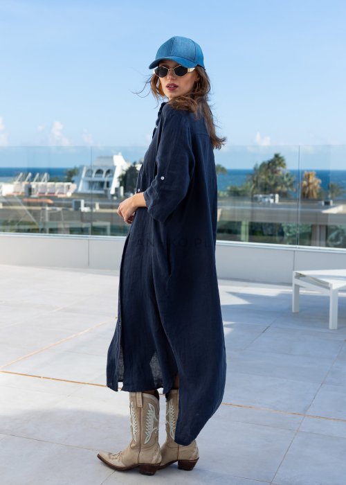 Granatowa lniana sukienka maxi w stylu szmizjerki, zapinana na guziki, o luźnym fasonie oversize, stylizowana z kowbojkami i czapką.