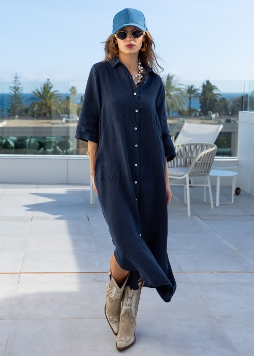 Granatowa lniana sukienka maxi w stylu szmizjerki, zapinana na guziki, o luźnym fasonie oversize, stylizowana z kowbojkami i czapką.