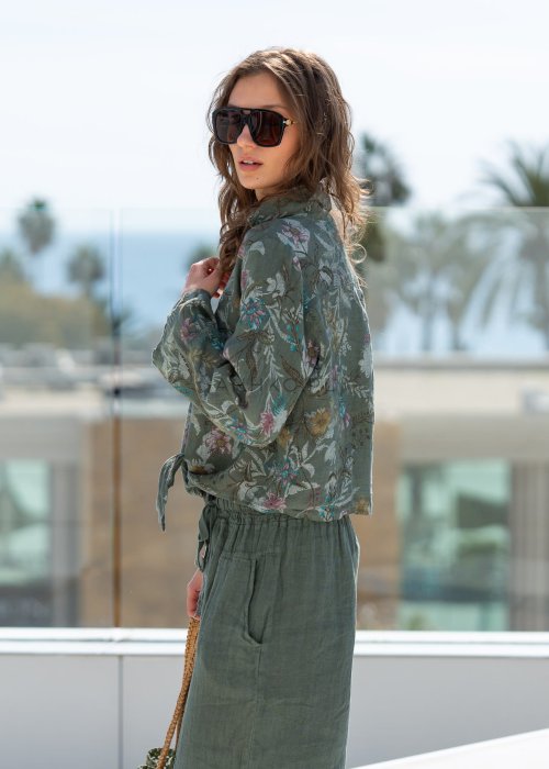 Lniana koszula damska w kolorze khaki z botanicznym printem w pastelowych barwach, o luźnym asymetrycznym kroju, zestawiona z lnianymi spodniami w tym samym odcieniu.