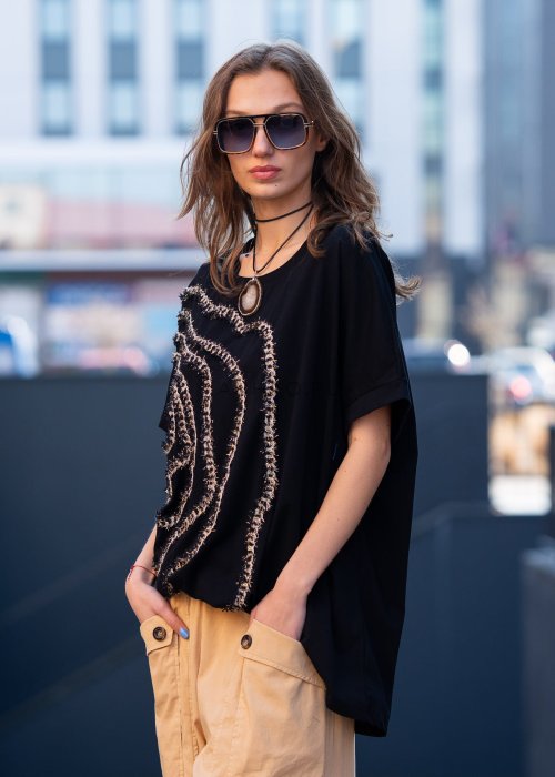 Czarna bluzka oversize damska z ozdobnym haftem 3D w kształcie spirali. Stylizacja casual z jasnymi spodniami i dodatkami w miejskim stylu.