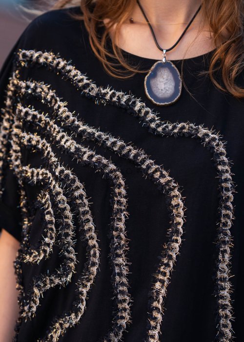 Czarna bluzka oversize damska z ozdobnym haftem 3D w kształcie spirali. Stylizacja casual z jasnymi spodniami i dodatkami w miejskim stylu.