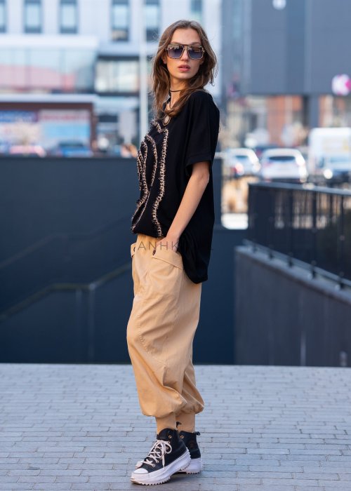 Czarna bluzka oversize damska z ozdobnym haftem 3D w kształcie spirali. Stylizacja casual z jasnymi spodniami i dodatkami w miejskim stylu.