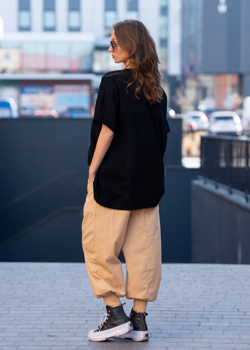 Czarna bluzka oversize damska z ozdobnym haftem 3D w kształcie spirali. Stylizacja casual z jasnymi spodniami i dodatkami w miejskim stylu.