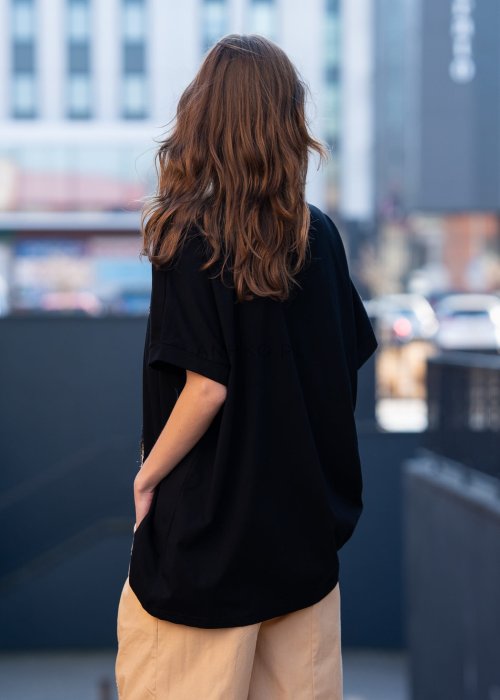 Czarna bluzka oversize damska z ozdobnym haftem 3D w kształcie spirali. Stylizacja casual z jasnymi spodniami i dodatkami w miejskim stylu.