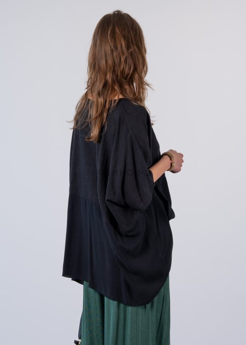 Czarna bluzka oversize z krótkim, szerokim rękawem i luźnym krojem. Stylizacja z zielonymi spodniami i minimalistyczną biżuterią.