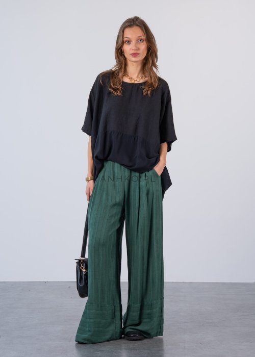 Czarna bluzka oversize z krótkim, szerokim rękawem i luźnym krojem. Stylizacja z zielonymi spodniami i minimalistyczną biżuterią.