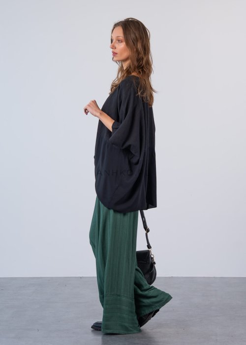 Czarna bluzka oversize z krótkim, szerokim rękawem i luźnym krojem. Stylizacja z zielonymi spodniami i minimalistyczną biżuterią.