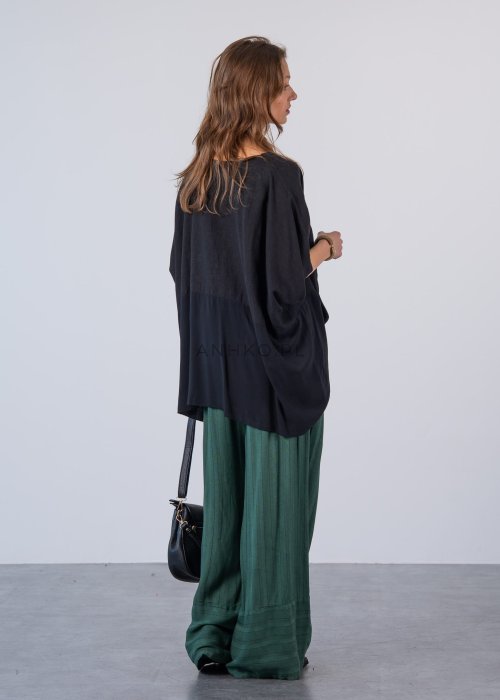 Czarna bluzka oversize z krótkim, szerokim rękawem i luźnym krojem. Stylizacja z zielonymi spodniami i minimalistyczną biżuterią.