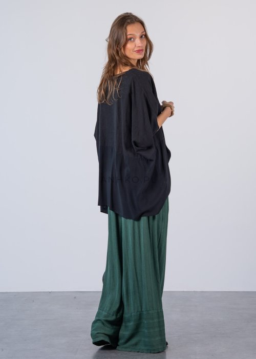 Czarna bluzka oversize z krótkim, szerokim rękawem i luźnym krojem. Stylizacja z zielonymi spodniami i minimalistyczną biżuterią.