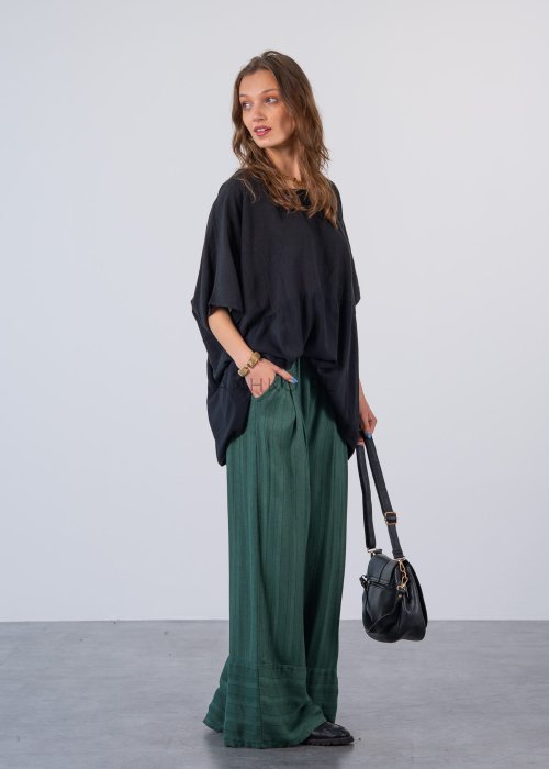 Czarna bluzka oversize z krótkim, szerokim rękawem i luźnym krojem. Stylizacja z zielonymi spodniami i minimalistyczną biżuterią.