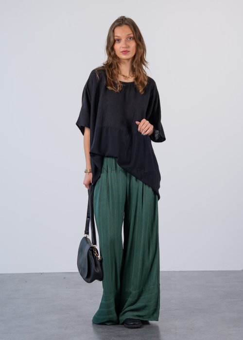 Czarna bluzka oversize z krótkim, szerokim rękawem i luźnym krojem. Stylizacja z zielonymi spodniami i minimalistyczną biżuterią.