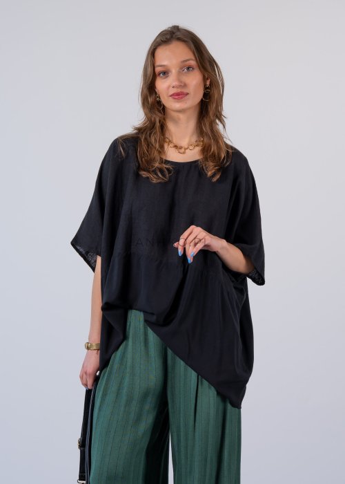 Czarna bluzka oversize z krótkim, szerokim rękawem i luźnym krojem. Stylizacja z zielonymi spodniami i minimalistyczną biżuterią.