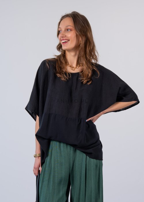 Czarna bluzka oversize z krótkim, szerokim rękawem i luźnym krojem. Stylizacja z zielonymi spodniami i minimalistyczną biżuterią.