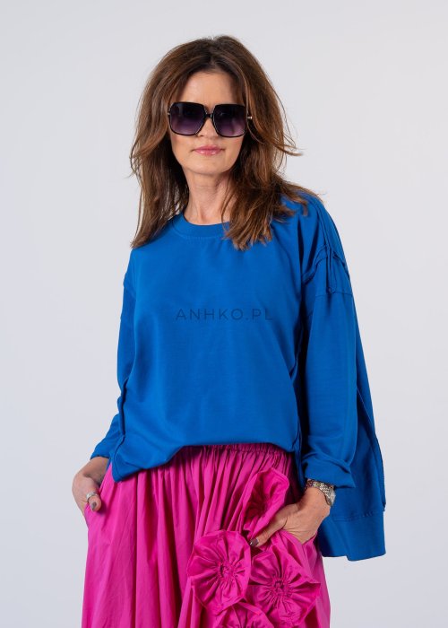 Damska bluza oversize w intensywnym niebieskim kolorze z długim rękawem i okrągłym dekoltem. Stylizacja zestawiona z różową spódnicą i okularami przeciwsłonecznymi.