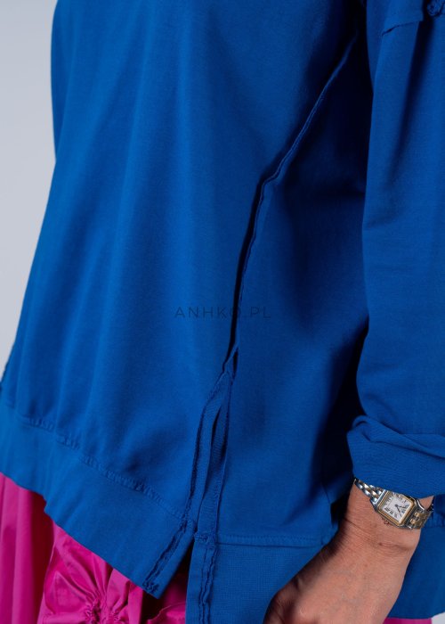 Damska bluza oversize w intensywnym niebieskim kolorze z długim rękawem i okrągłym dekoltem. Stylizacja zestawiona z różową spódnicą i okularami przeciwsłonecznymi.