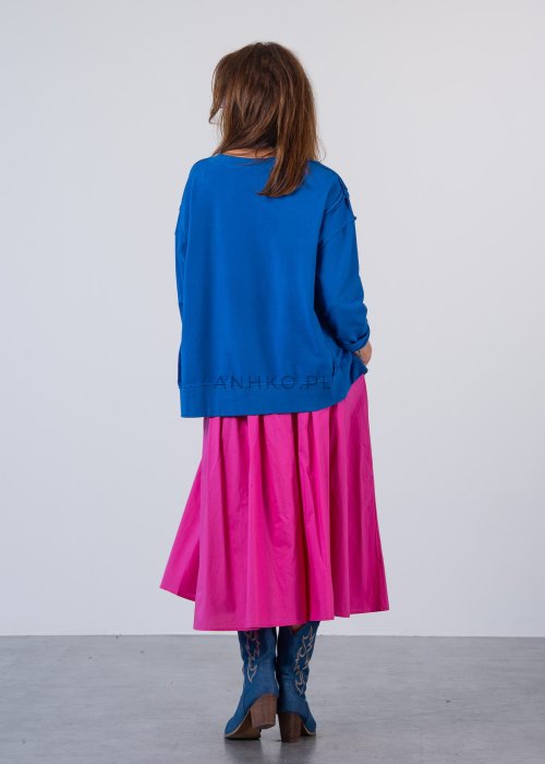 Damska bluza oversize w intensywnym niebieskim kolorze z długim rękawem i okrągłym dekoltem. Stylizacja zestawiona z różową spódnicą i okularami przeciwsłonecznymi.