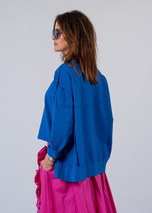Damska bluza oversize w intensywnym niebieskim kolorze z długim rękawem i okrągłym dekoltem. Stylizacja zestawiona z różową spódnicą i okularami przeciwsłonecznymi.