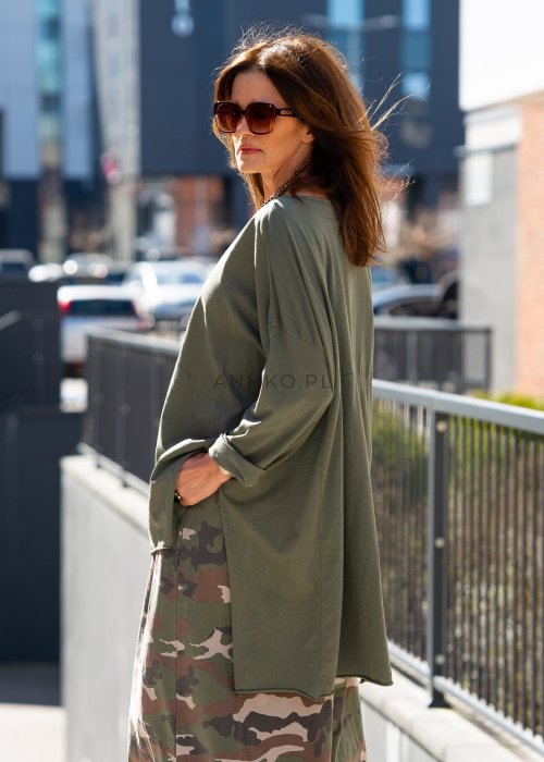 Ciemnozielona bluza damska oversize z asymetrycznym dołem i długim rękawem. Model o luźnym kroju pokazany w stylizacji z długą spódnicą moro w miejskim looku.