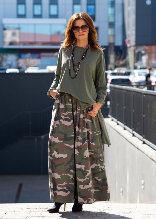 Ciemnozielona bluza damska oversize z asymetrycznym dołem i długim rękawem. Model o luźnym kroju pokazany w stylizacji z długą spódnicą moro w miejskim looku.