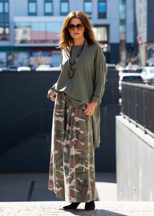 Ciemnozielona bluza damska oversize z asymetrycznym dołem i długim rękawem. Model o luźnym kroju pokazany w stylizacji z długą spódnicą moro w miejskim looku.