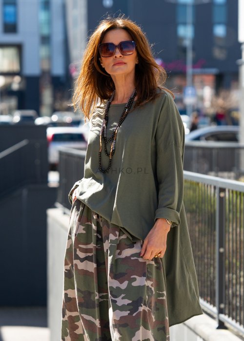 Ciemnozielona bluza damska oversize z asymetrycznym dołem i długim rękawem. Model o luźnym kroju pokazany w stylizacji z długą spódnicą moro w miejskim looku.