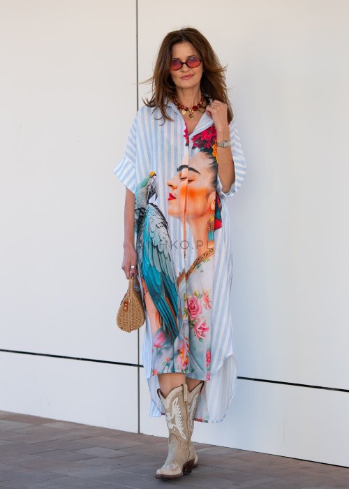 Lniana sukienka maxi w błękitne paski z artystycznym nadrukiem kobiety, papugi i kwiatów, noszona z kowbojkami i torebką w stylu boho.