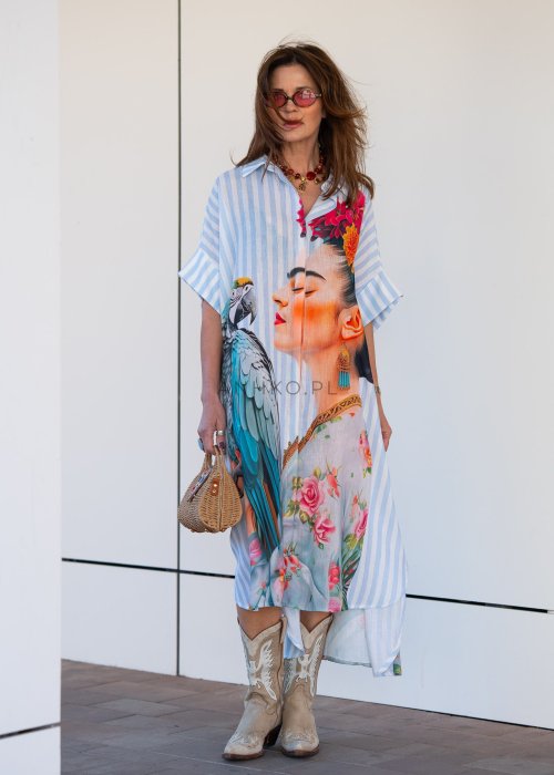Lniana sukienka maxi w błękitne paski z artystycznym nadrukiem kobiety, papugi i kwiatów, noszona z kowbojkami i torebką w stylu boho.