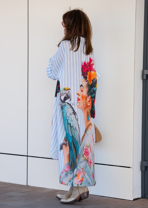 Lniana sukienka maxi w błękitne paski z artystycznym nadrukiem kobiety, papugi i kwiatów, noszona z kowbojkami i torebką w stylu boho.