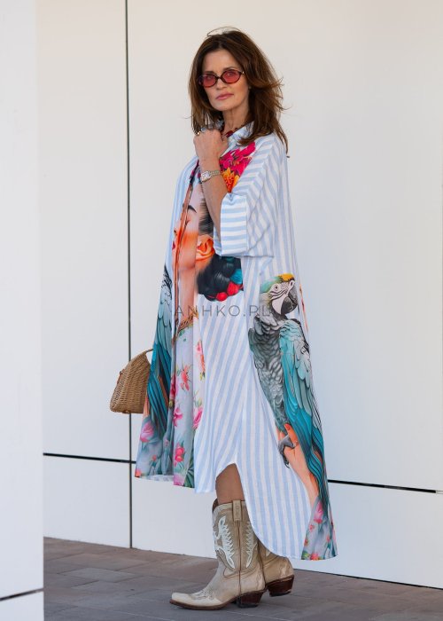 Lniana sukienka maxi w błękitne paski z artystycznym nadrukiem kobiety, papugi i kwiatów, noszona z kowbojkami i torebką w stylu boho.