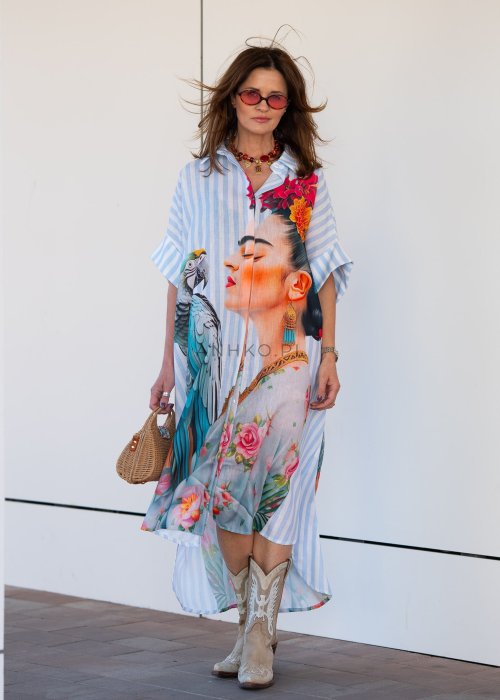 Lniana sukienka maxi w błękitne paski z artystycznym nadrukiem kobiety, papugi i kwiatów, noszona z kowbojkami i torebką w stylu boho.