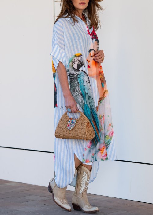 Lniana sukienka maxi w błękitne paski z artystycznym nadrukiem kobiety, papugi i kwiatów, noszona z kowbojkami i torebką w stylu boho.