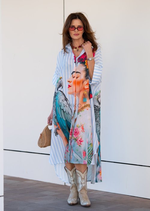 Lniana sukienka maxi w błękitne paski z artystycznym nadrukiem kobiety, papugi i kwiatów, noszona z kowbojkami i torebką w stylu boho.