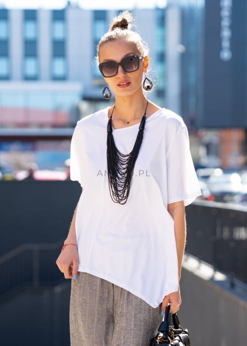 Biała bluzka damska o luźnym, asymetrycznym kroju z krótkim rękawem. Model prezentowany w stylizacji z szerokimi spodniami, podkreślającej nowoczesny i minimalistyczny charakter fasonu.