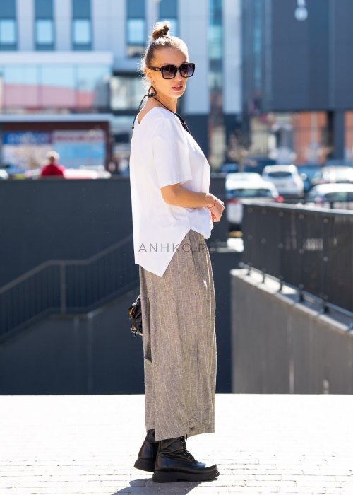 Biała bluzka damska o luźnym, asymetrycznym kroju z krótkim rękawem. Model prezentowany w stylizacji z szerokimi spodniami, podkreślającej nowoczesny i minimalistyczny charakter fasonu.