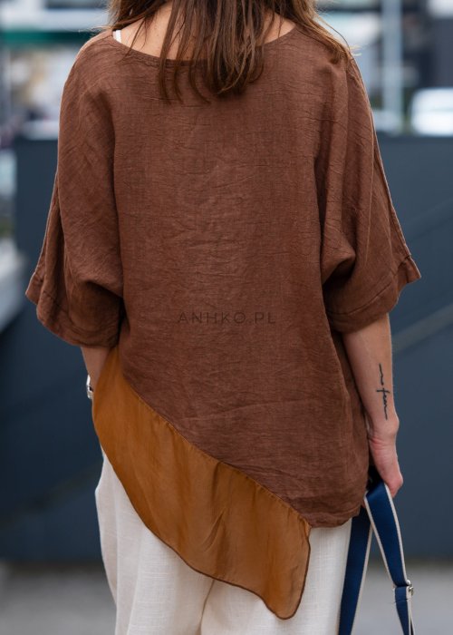 Brązowa bluzka lniana oversize z asymetrycznym dołem i lekką, transparentną wstawką, zestawiona z jasnymi spodniami w miejskiej stylizacji.
