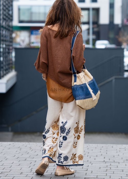 Brązowa bluzka lniana oversize z asymetrycznym dołem i lekką, transparentną wstawką, zestawiona z jasnymi spodniami w miejskiej stylizacji.