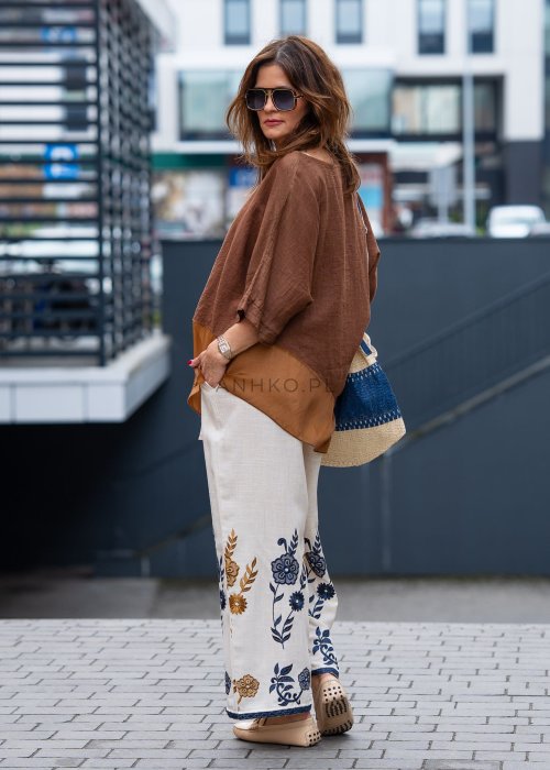 Brązowa bluzka lniana oversize z asymetrycznym dołem i lekką, transparentną wstawką, zestawiona z jasnymi spodniami w miejskiej stylizacji.