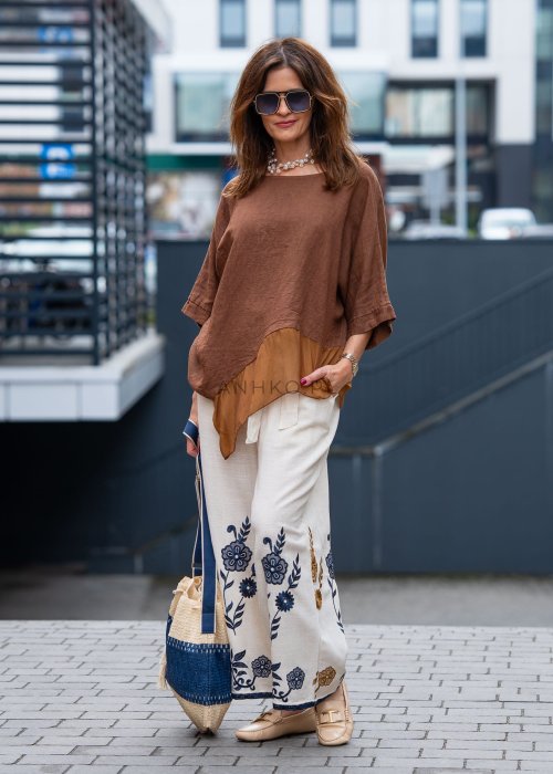 Brązowa bluzka lniana oversize z asymetrycznym dołem i lekką, transparentną wstawką, zestawiona z jasnymi spodniami w miejskiej stylizacji.