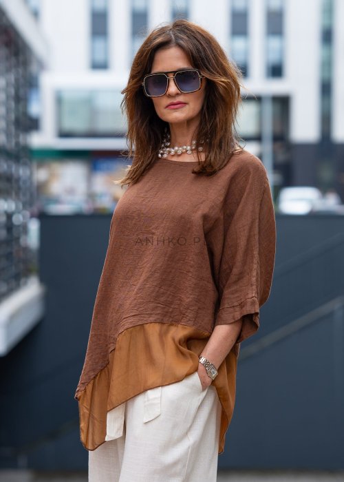 Brązowa bluzka lniana oversize z asymetrycznym dołem i lekką, transparentną wstawką, zestawiona z jasnymi spodniami w miejskiej stylizacji.