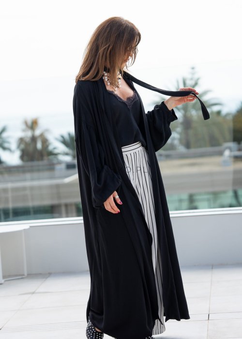 Czarne kimono damskie maxi o długim, lejącym fasonie z bufiastymi rękawami. Stylizacja z topem i szerokimi spodniami w kontrastowe paski.