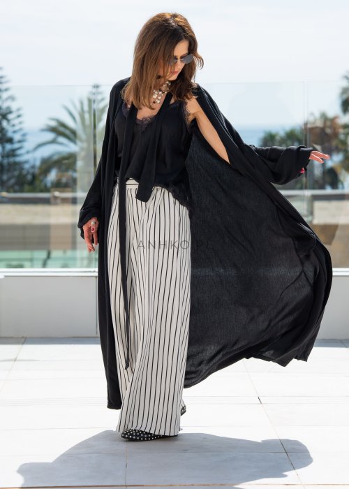 Czarne kimono damskie maxi o długim, lejącym fasonie z bufiastymi rękawami. Stylizacja z topem i szerokimi spodniami w kontrastowe paski.