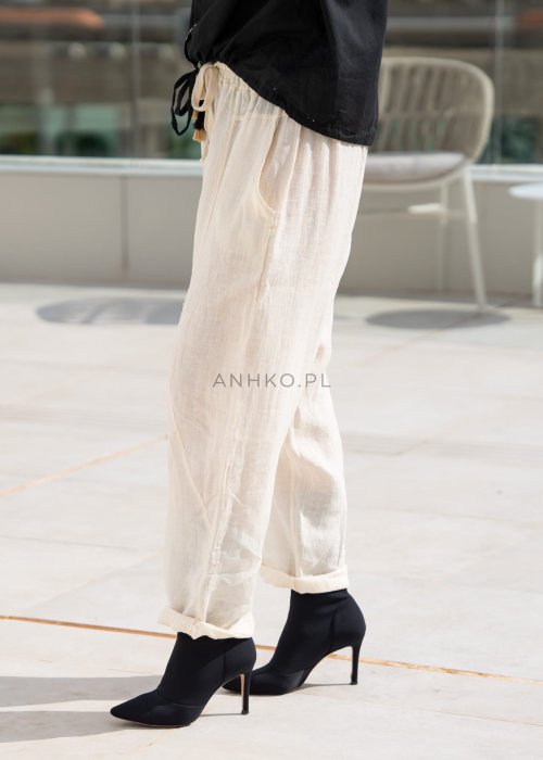 Śmietankowe spodnie lniane damskie o luźnym kroju RelaxFit z elastycznym pasem i troczkiem, stylizowane z czarną koszulą i botkami w eleganckim, minimalistycznym looku.