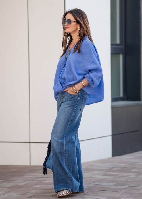 Niebieska koszula lniana oversize z dekoltem V i guzikami, stylizowana z jeansami.