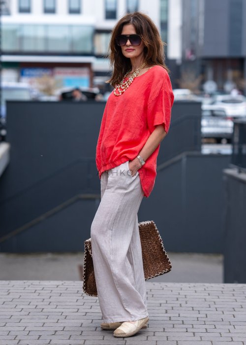 Koralowa lniana bluzka oversize ze ściągaczem u dołu, stylizowana z biżuterią i miejskim outfitem w energetycznym wydaniu.