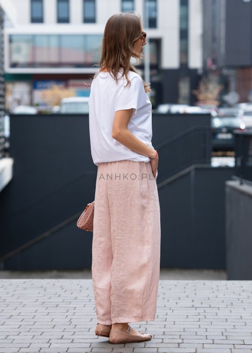 Jasnoróżowe lniane spodnie damskie z szeroką nogawką i elastycznym pasem ze sznurkiem. Stylizacja casual z białą bluzką i balerinami.