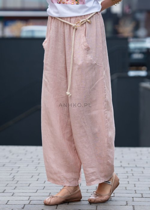 Jasnoróżowe lniane spodnie damskie z szeroką nogawką i elastycznym pasem ze sznurkiem. Stylizacja casual z białą bluzką i balerinami.