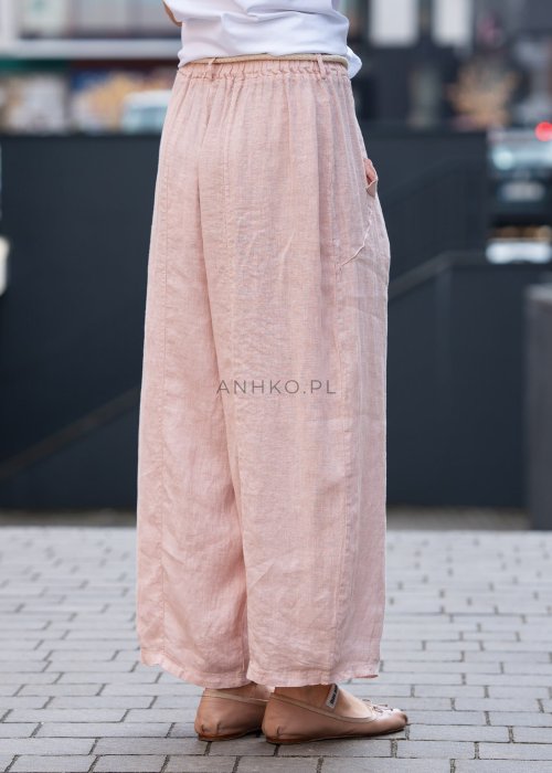 Jasnoróżowe lniane spodnie damskie z szeroką nogawką i elastycznym pasem ze sznurkiem. Stylizacja casual z białą bluzką i balerinami.